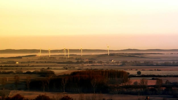 A large wind farm at sunset, with wind turbines spinning and providing clean energy, symbolizing the shift towards renewable energy sources.
